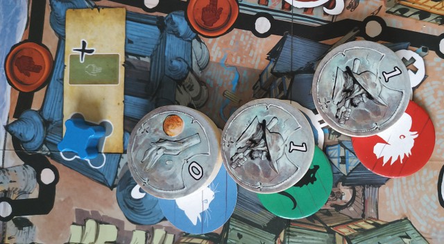 Les Clans rouge (Marfaux) et vert (Malingreux) ont la même force de combat. C’est le joueur le plus proche de la croix blanche (à droite) qui remporte l’Affrontement. Le joueur rouge posera donc son pion Renommée à la place de celui du joueur bleu (Orphelin) dans le cartouche du quartier)