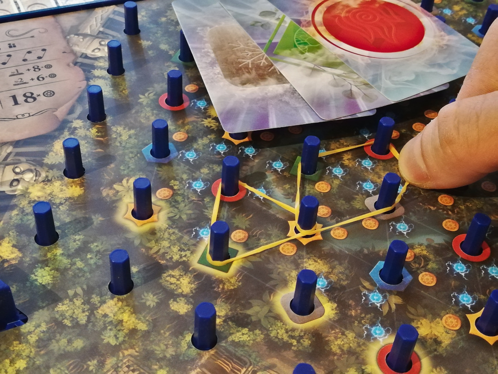 Le premier élastique posé doit toucher un picot brillant en bord de plateau. Les suivants devront toucher un picot que vous contrôlez déjà. Ici pour poser ce 2e élastique, je ne paye que 3 cartes verte, grise et rouge, car je possède déjà le picot orange.