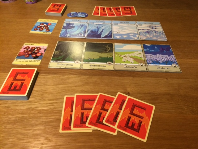 Une fois le jeu mis en place. "Lieux" placés sur deux rangées de 4 colonnes. La carte "héros" à gauche, le deck en-dessous et la main de départ.